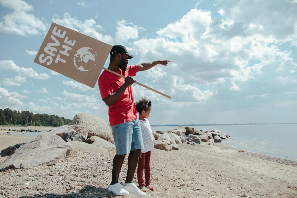 Father and child holding a 'Save the Earth' sign during a beach cleanup event.